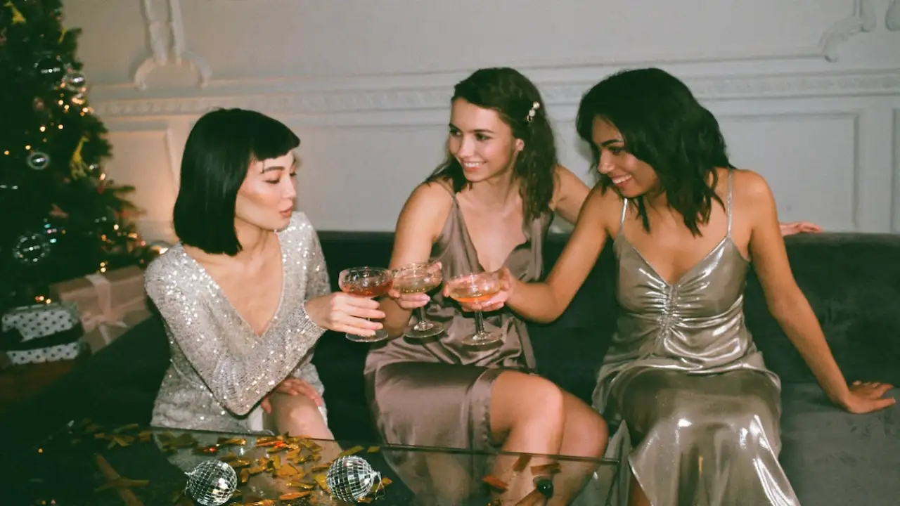 Three women sitting on a sofa enjoying drinks  wearing party dresses from Black Friday Deals that are screaming for your attention